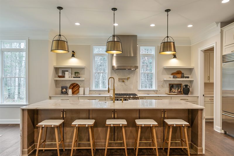 Staged kitchen with a marble island, five counter stools and three lantern pendants