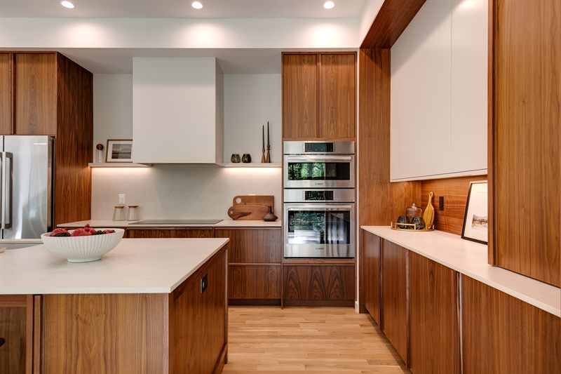 Walnut kitchen with a white quartz island, double wall ovens and a bowl of fruit on the counter