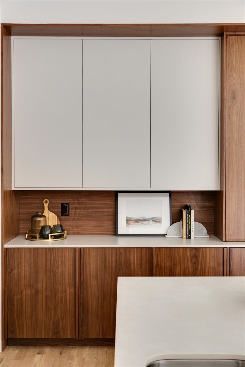 Walnut coffee bar with white cabinets above, canisters on a brass tray and a small framed landscape