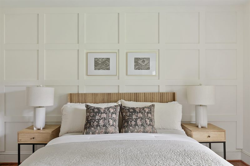 Bedroom with a panelled white wall, slatted wood headboard, matching lamps and two framed prints