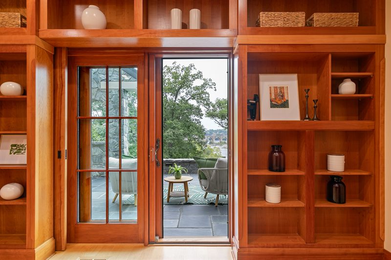 Cherry built-in shelving framing a glass door that opens onto a stone terrace