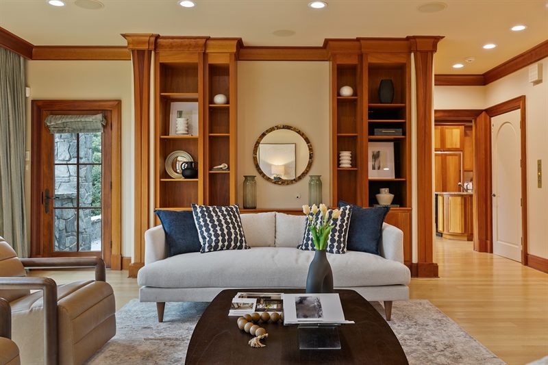 Living room with a cream sofa between cherry built-ins, navy pillows and a round mirror above