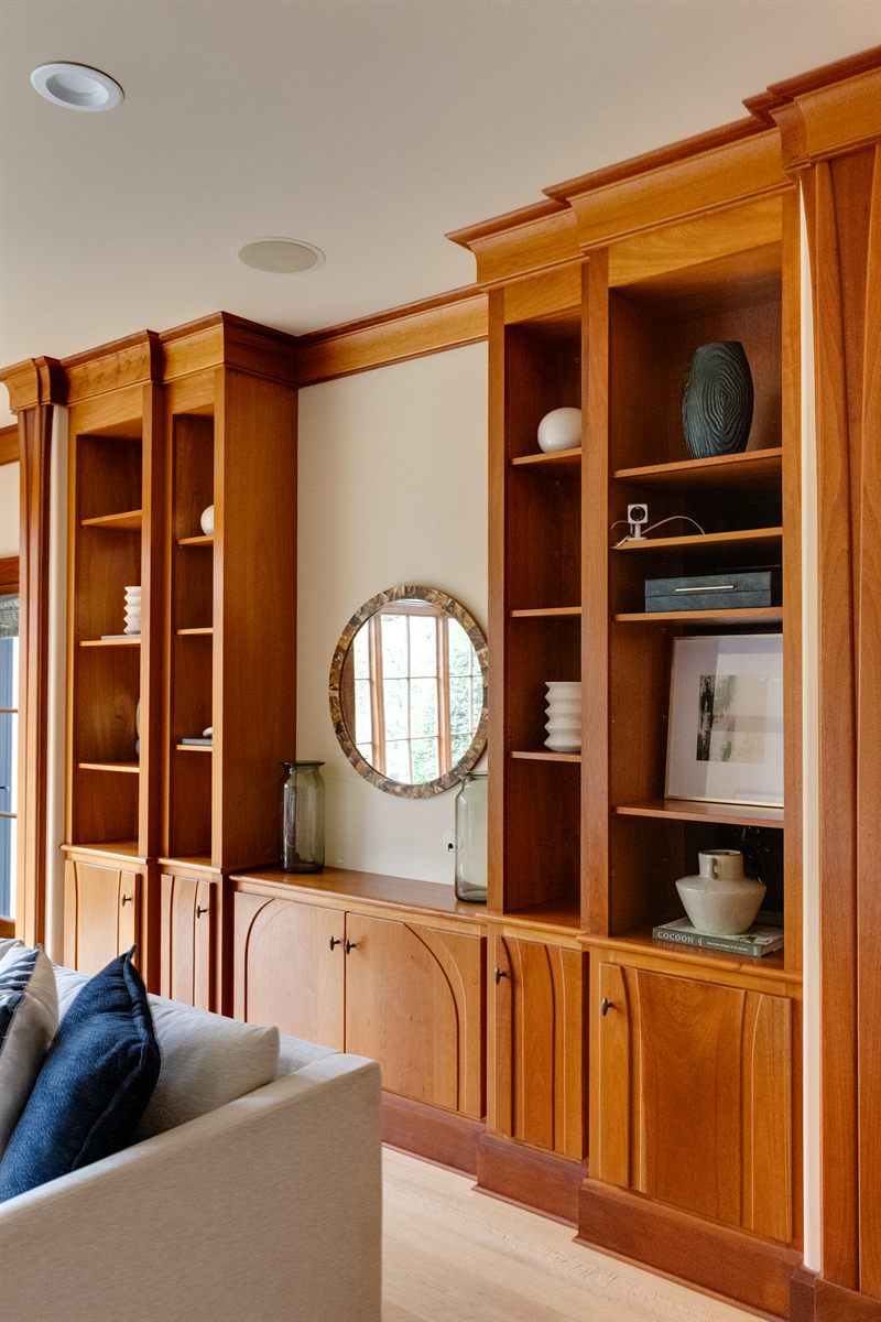Tall cherry built-in bookcases styled with pottery and books beside an oval mirror
