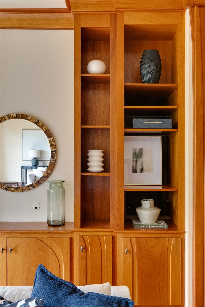 Cherry shelves styled with a ribbed vase, framed art and a green glass jar beside an oval mirror