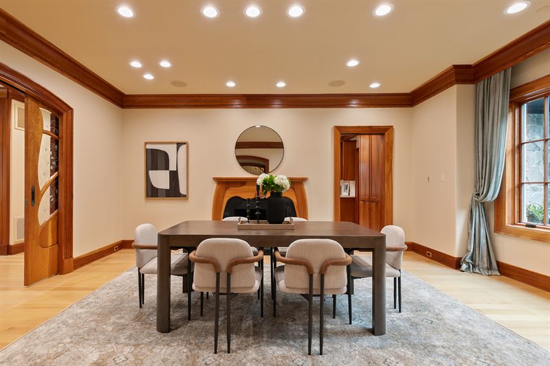 Dining room with a dark wood table, cream chairs and an arched mirror above the mantel
