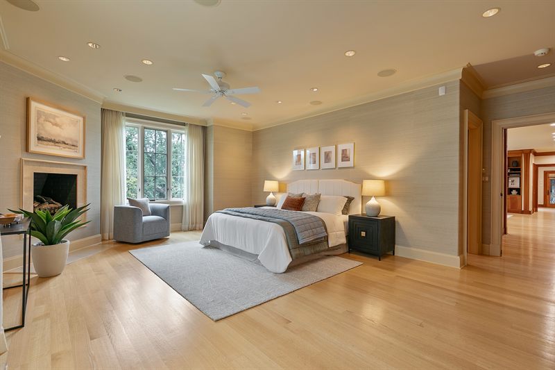 Large primary bedroom with a fireplace, upholstered bed, grey rug and an armchair in the corner