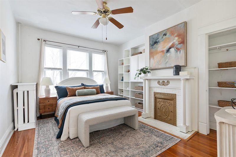 Bedroom with an arched headboard, upholstered bench and abstract art above a white fireplace mantel