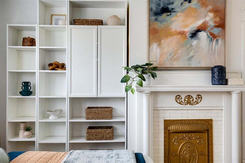 White built-in shelving with baskets beside a brick fireplace under a large abstract canvas