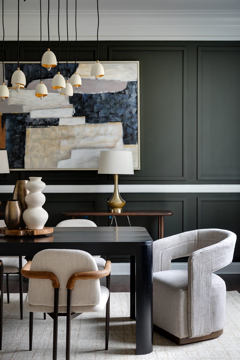 Dining room with deep green panelled walls, a black table and a cluster of pendant lights