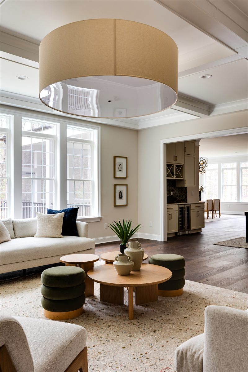 Living room under a large drum pendant, with a cream sofa, round wood table and green velvet ottomans