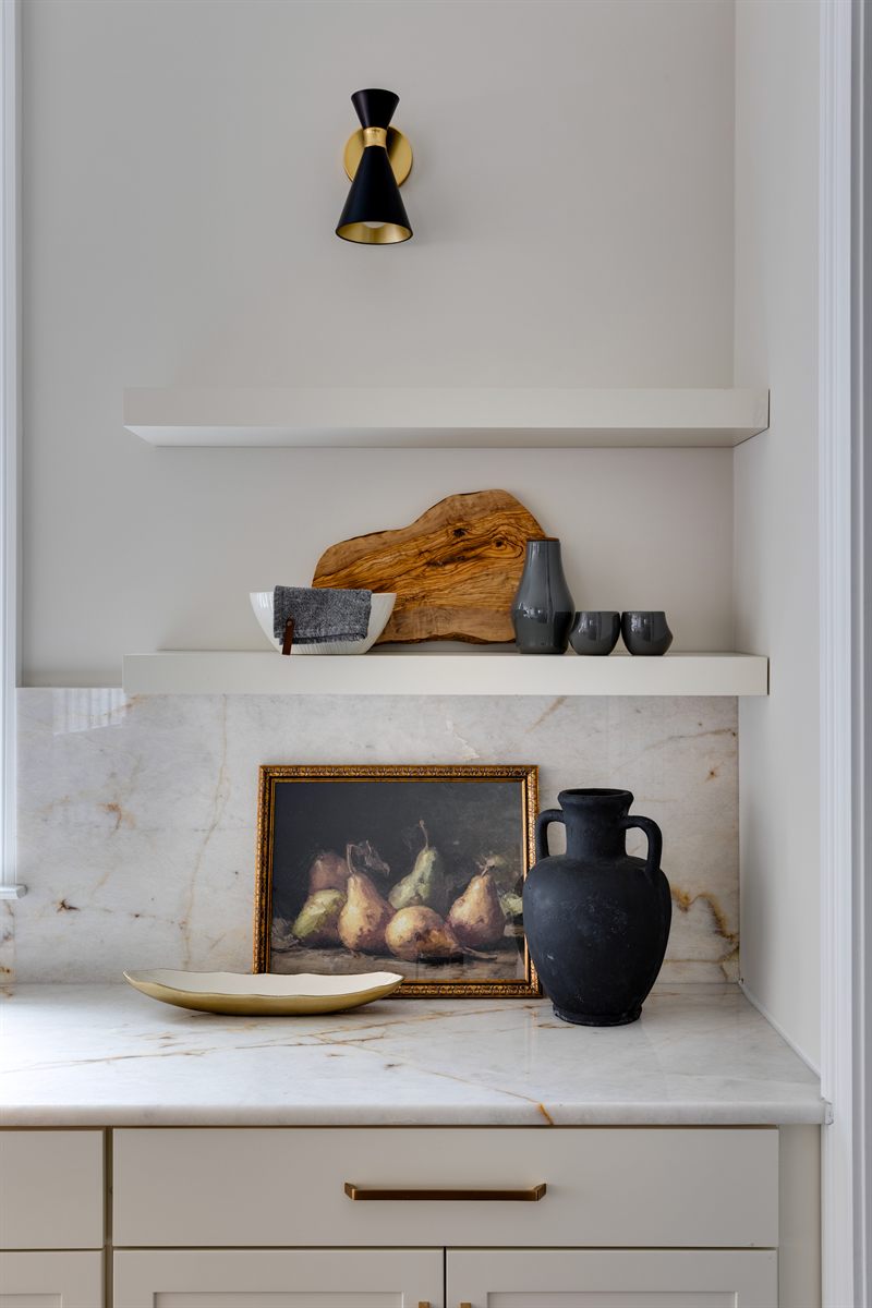 Kitchen vignette with a gilt still life, black urn and brass tray against a marble backsplash