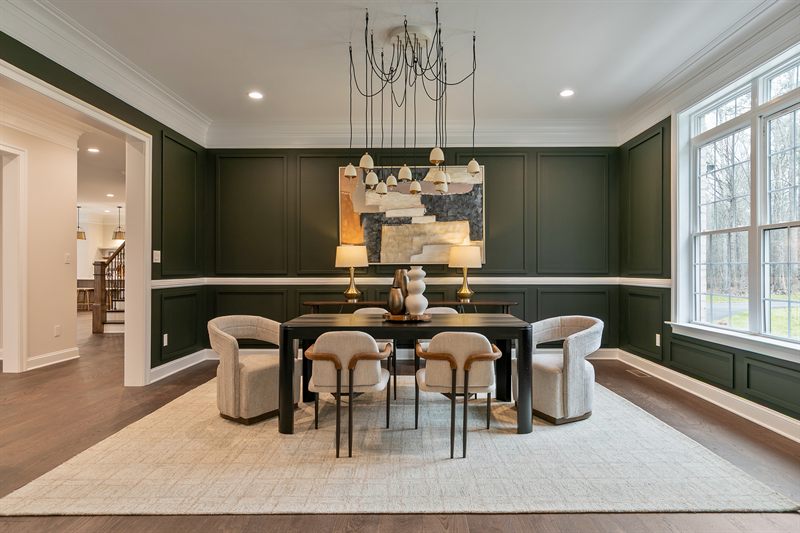 Dining room with dark green panelled walls, a sculptural chandelier and cream barrel chairs