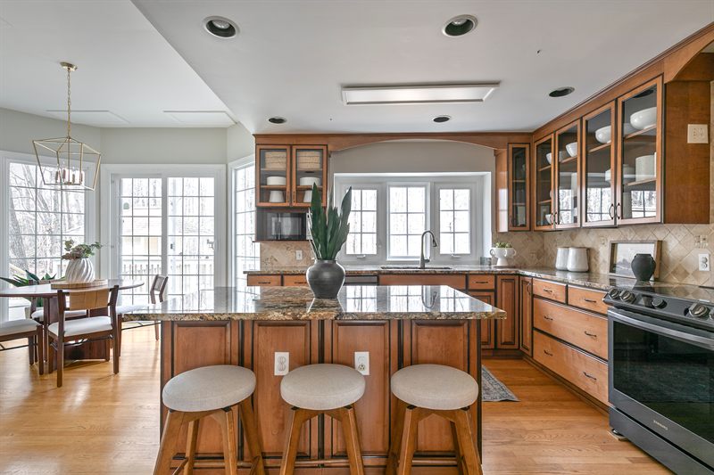 Kitchen with maple cabinets, a granite island with three stools and a breakfast table beyond