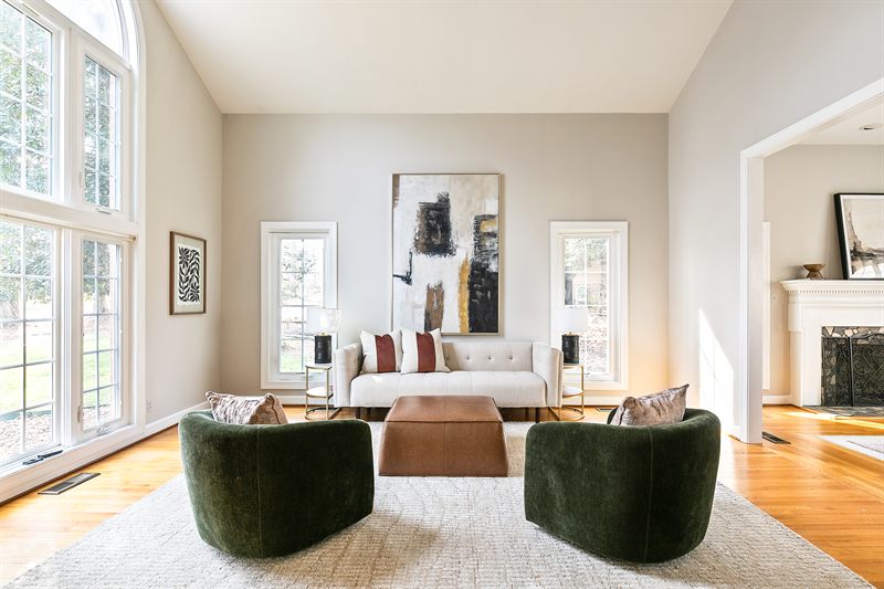 Living room with two-storey windows, deep green swivel chairs and a leather ottoman
