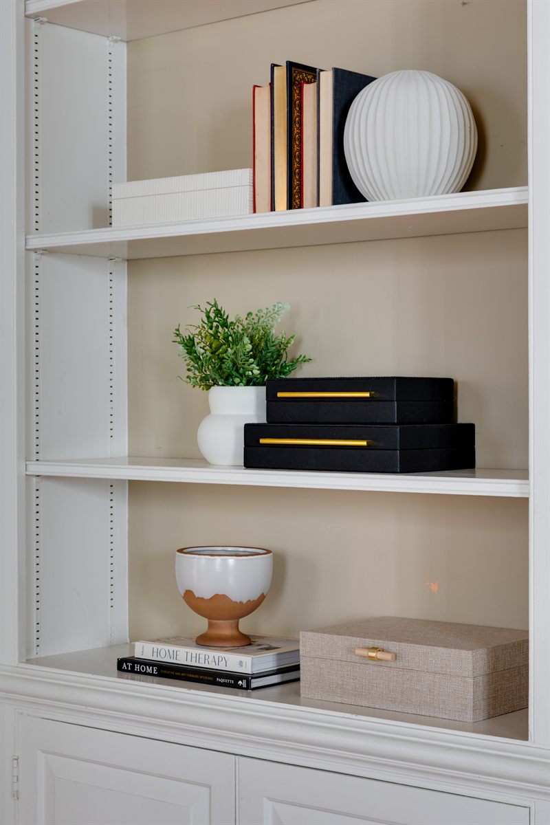 White built-in shelves styled with books, black boxes, a small plant and a linen box