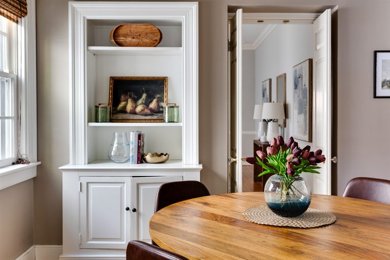 Round breakfast table with tulips beside a built-in cabinet holding a framed still life