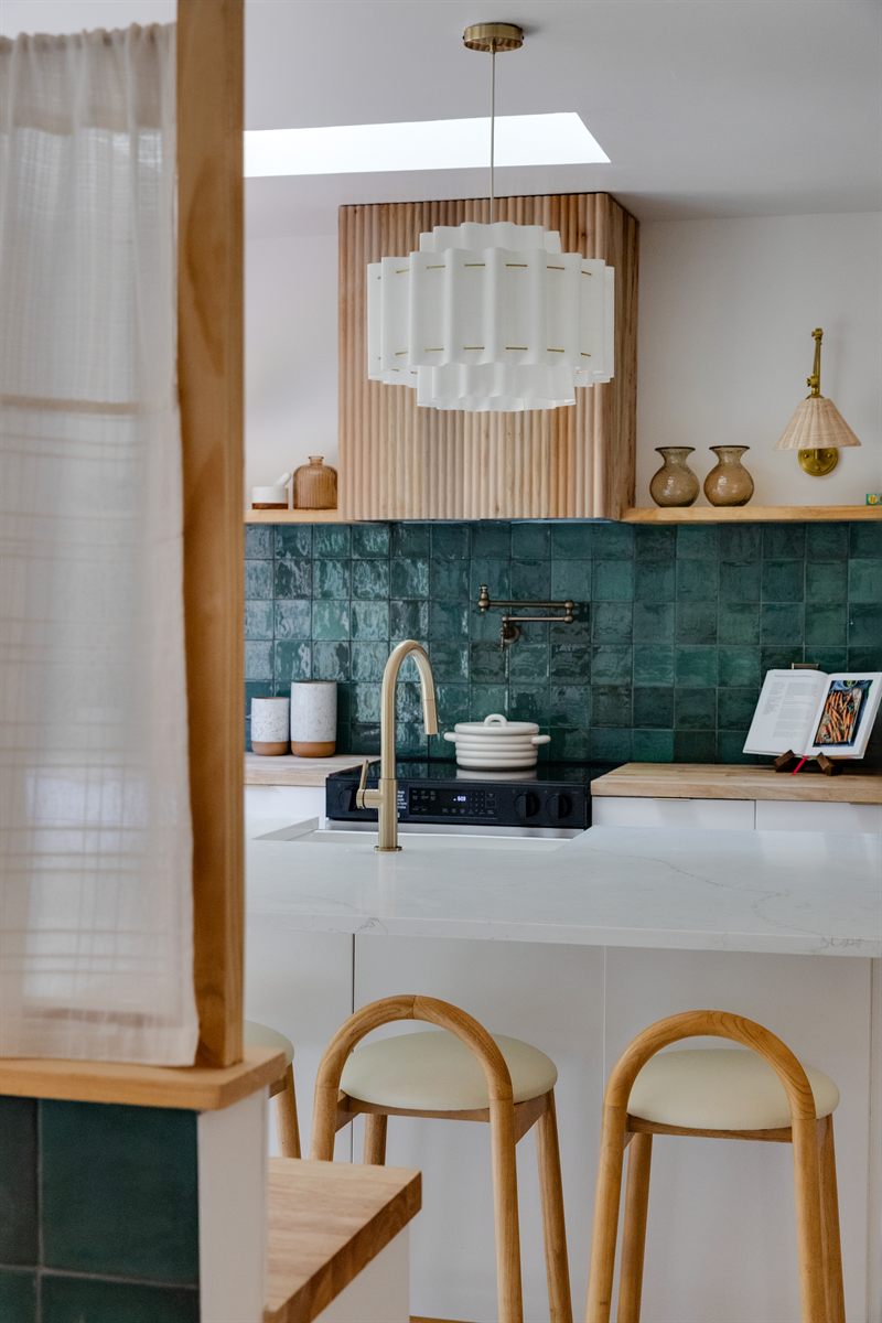 Kitchen with green zellige tile, a brass pot filler and wood stools at a white waterfall island