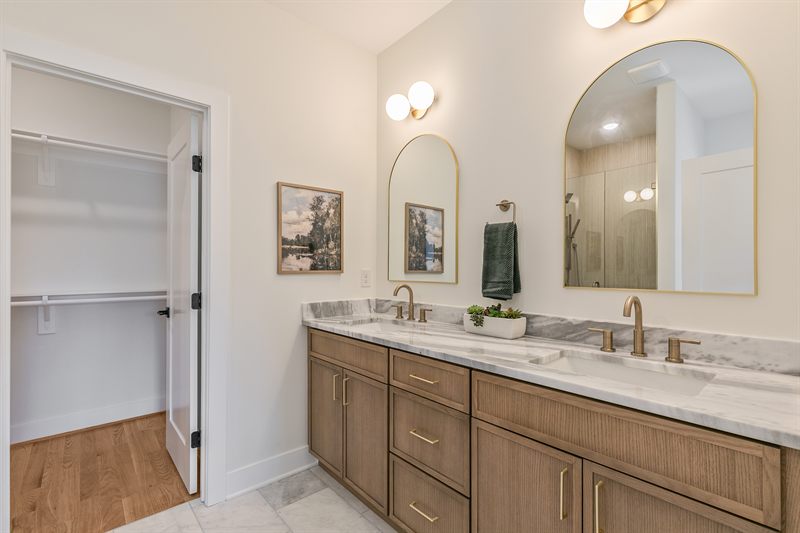 Primary bathroom with a double oak vanity, two arched gilt mirrors and a walk-in closet beyond