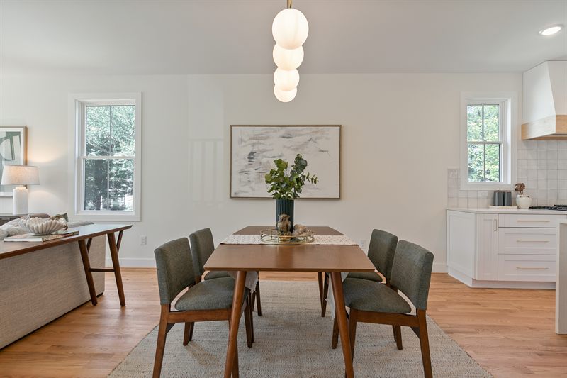 Dining room with a cluster of globe pendants, green upholstered chairs and a framed landscape