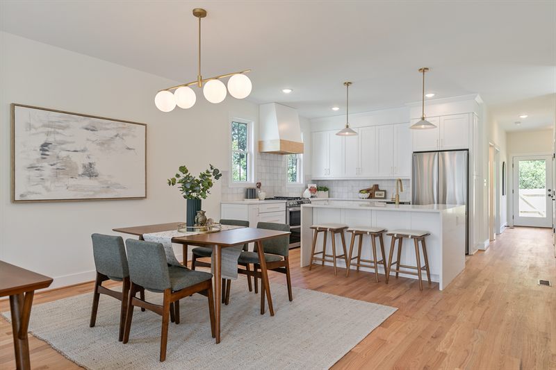 Open-plan dining table with green chairs under globe pendants, looking through to the white kitchen