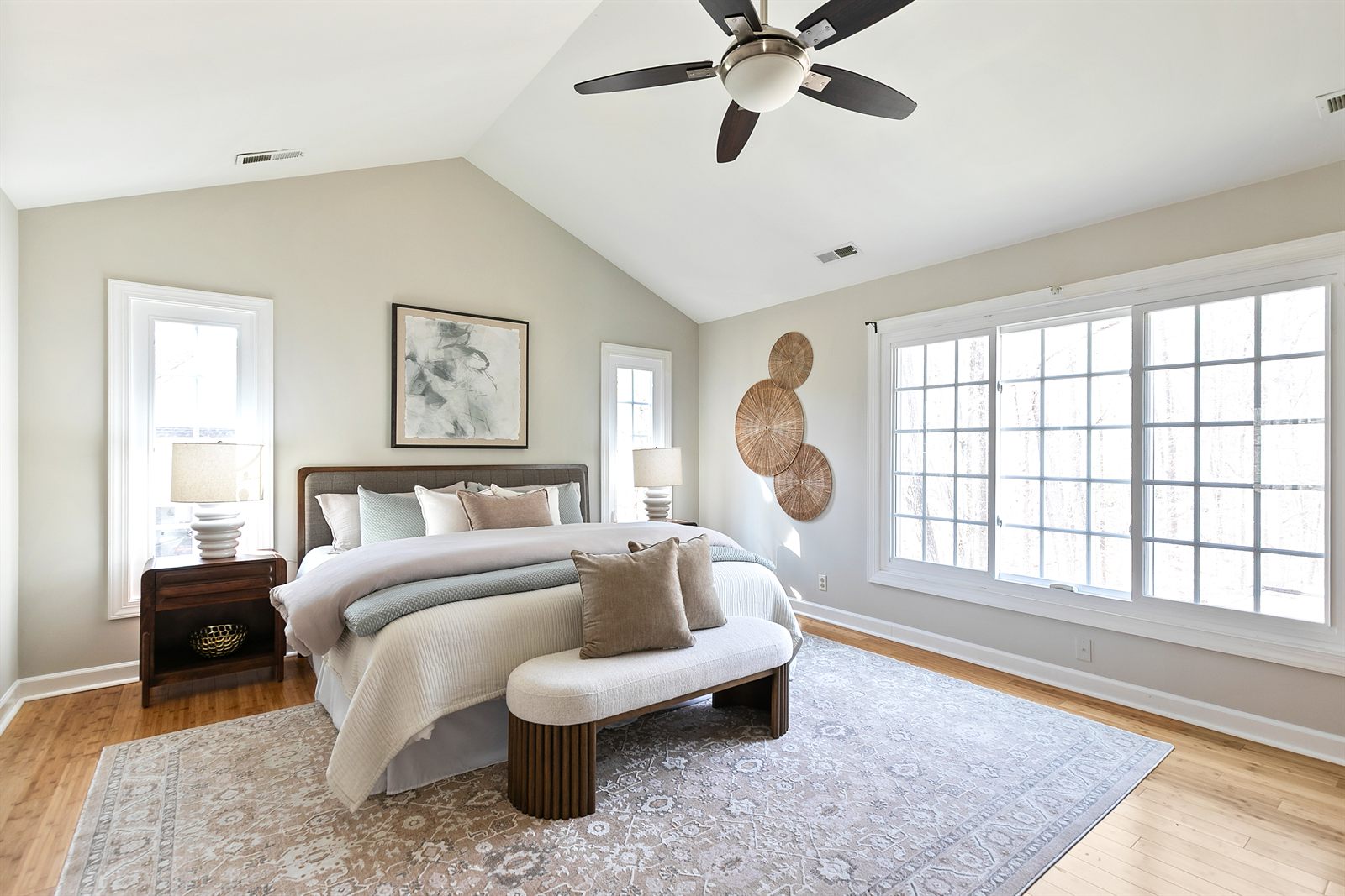 Staged primary bedroom with a vaulted ceiling, upholstered bed and a bench at its foot